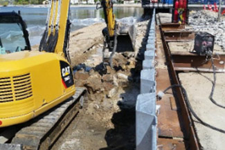 Excavator installing riprap to protect a retaining wall